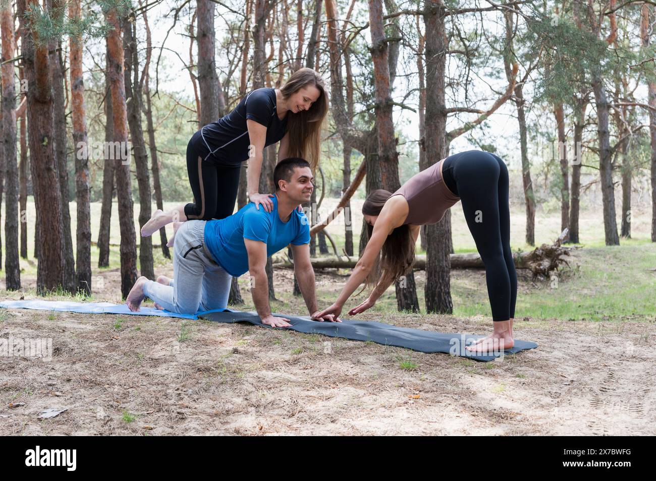 Drei Freunde üben Akro-Yoga-Übungen im Wald. Der Mann ist auf allen Vieren. Das Mädchen ist auf dem Rücken. Stockfoto
