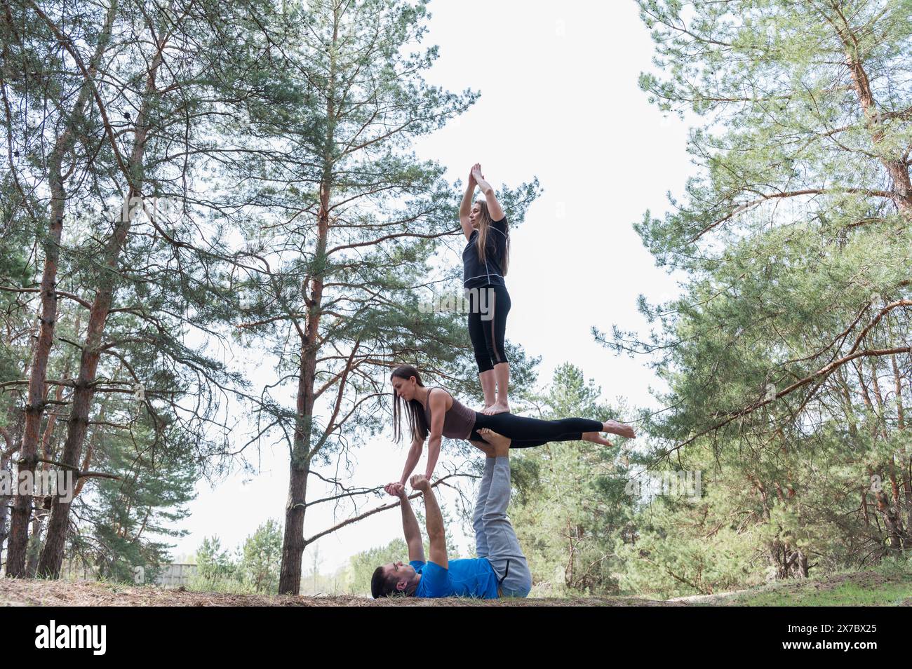 Drei Freunde üben Acro-Yoga-Übungen beim Wandern im Wald. Stockfoto