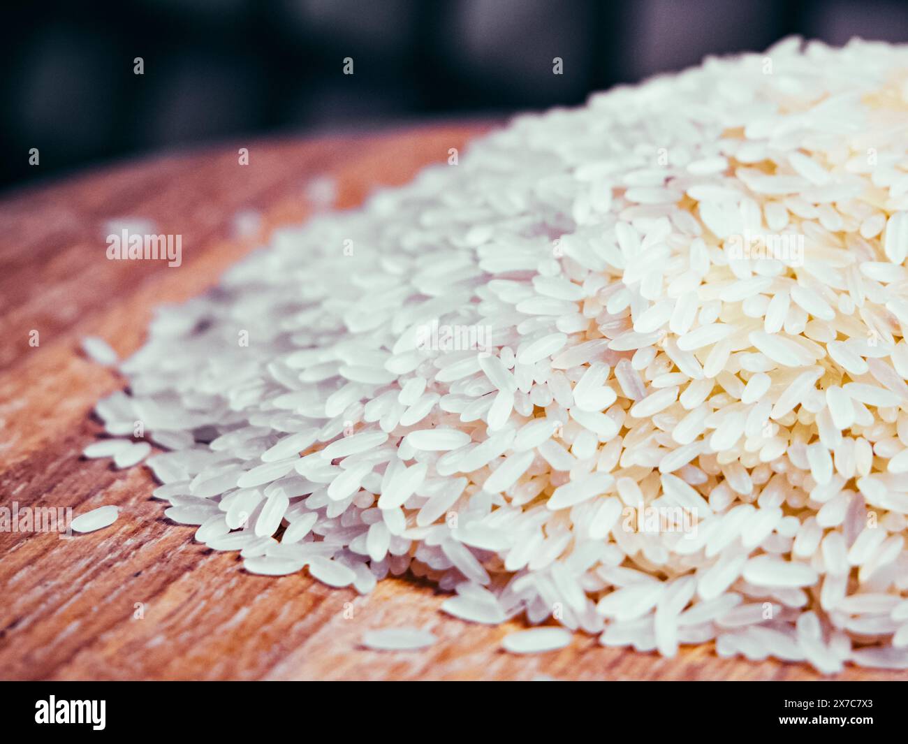 Weiße Reiskörner auf Holz, verschwommener Hintergrund, einfaches Bild zum Kochen oder zum Einkaufen. Stockfoto