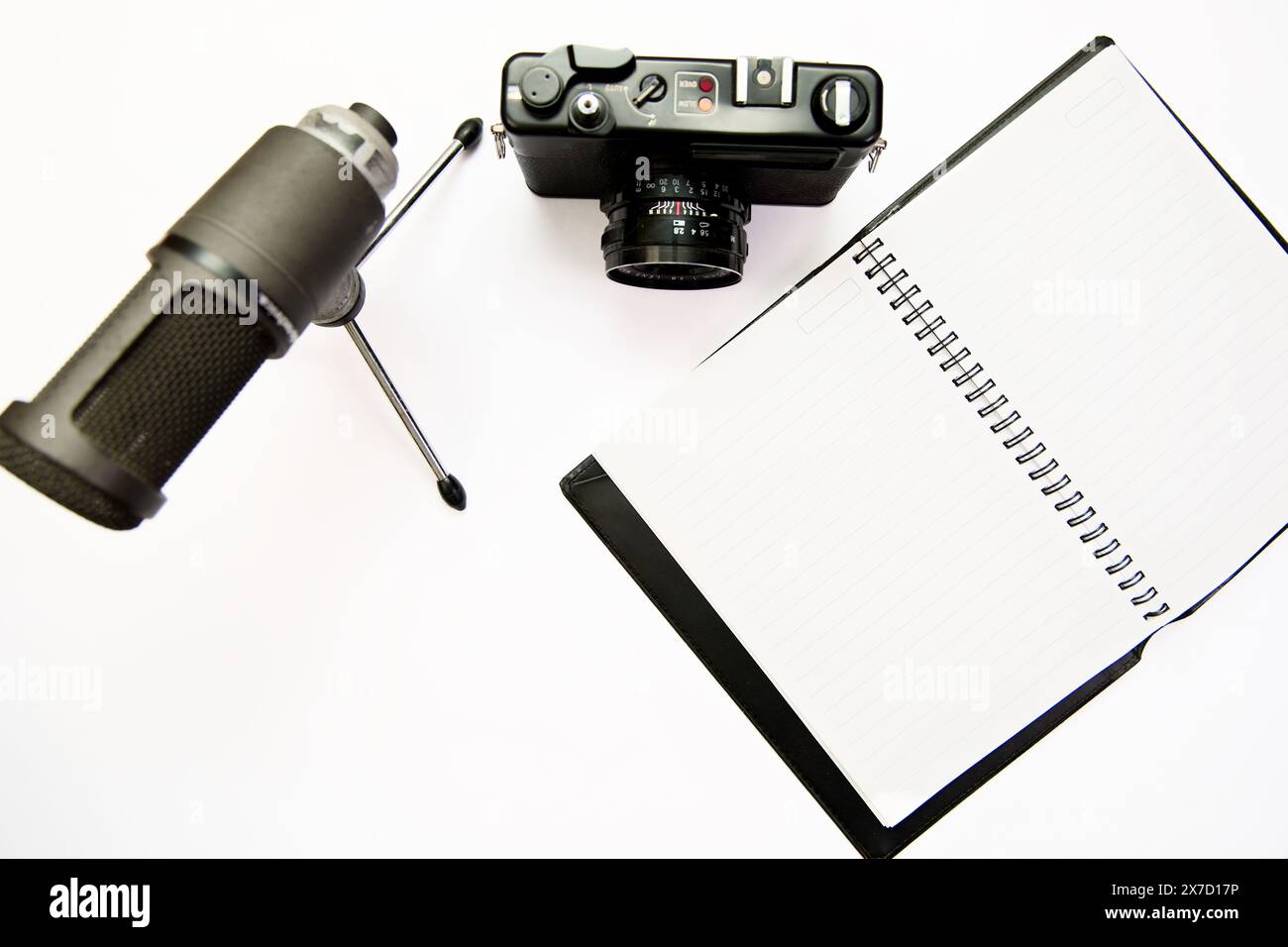 Fotokamera, Mikrofon und Notizblock auf einem sauberen weißen Hintergrund. Perfekt für die Darstellung von Content Creation, Vlogging, Journalismus oder Schreiben. Stockfoto