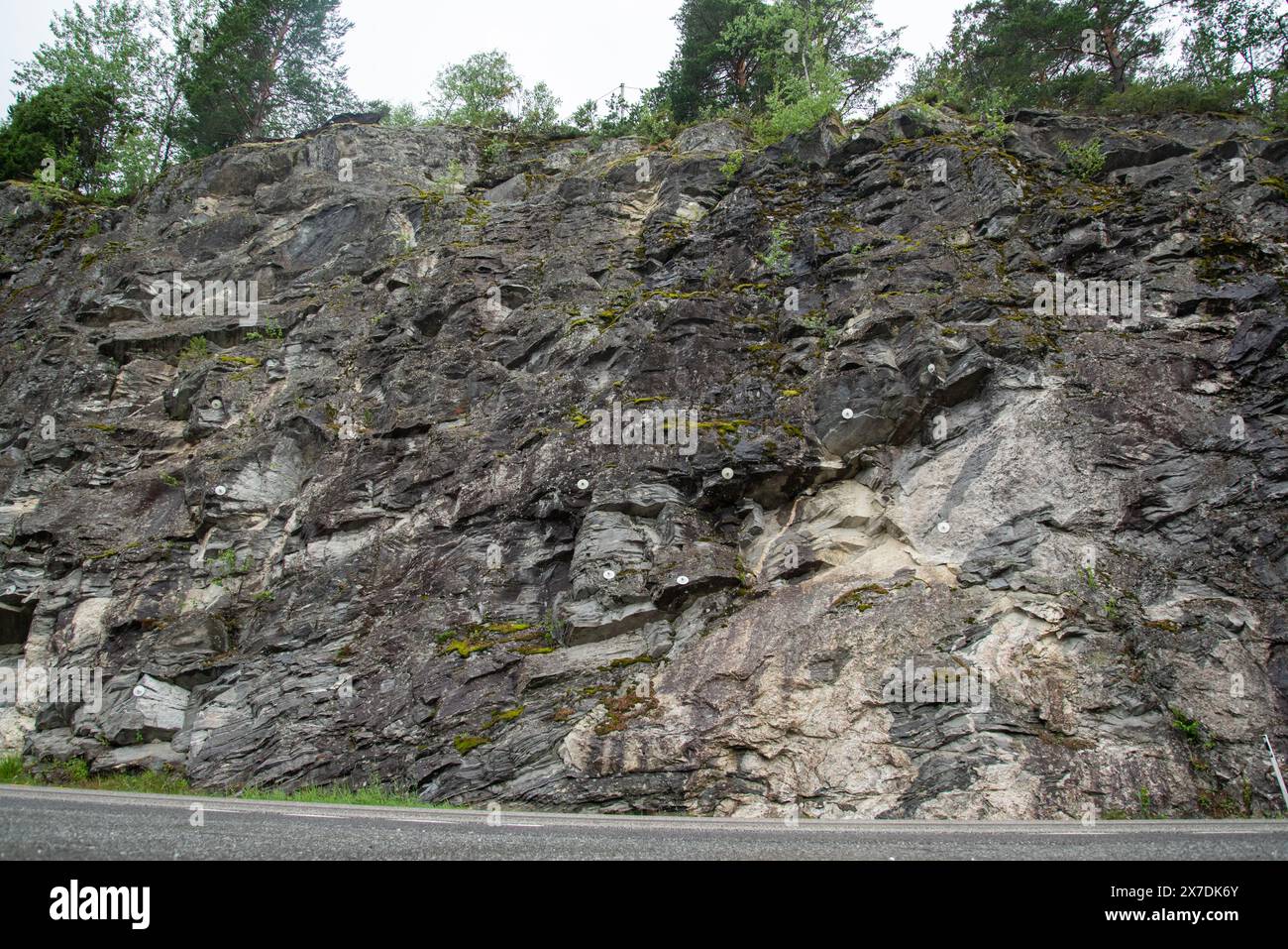 Steinsteinmauer neben einer Bergstraße, in die Metallbefestigungen gebohrt wurden, um die Felsen zu schützen. Stockfoto