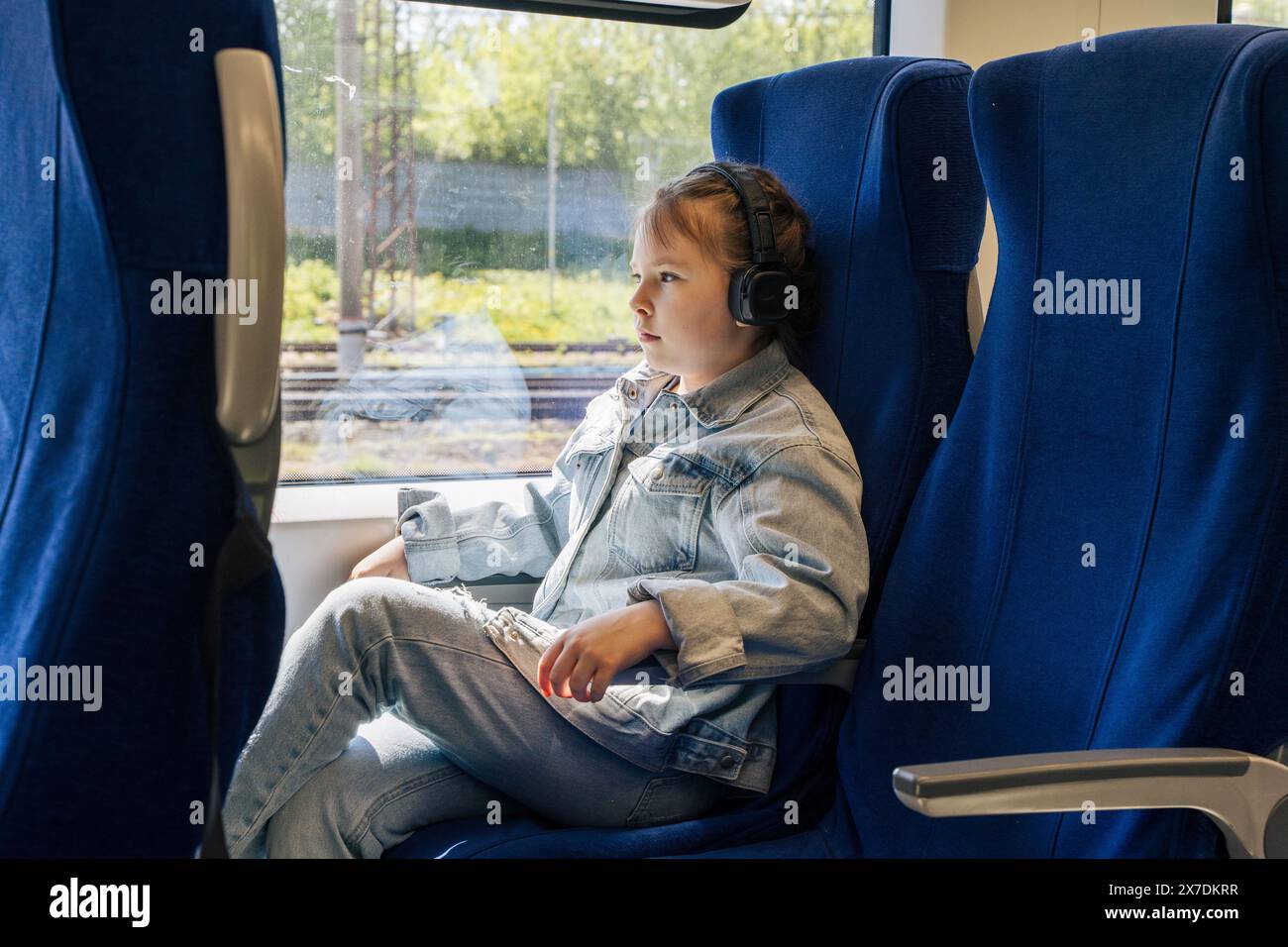 Entspannen Sie sich im Zug. Das Mädchen reist in einem Fern- und Kurzstreckenzug mit nachdenklichem Gesicht und hört Musik in Kopfhörern. Wählen Sie Stockfoto