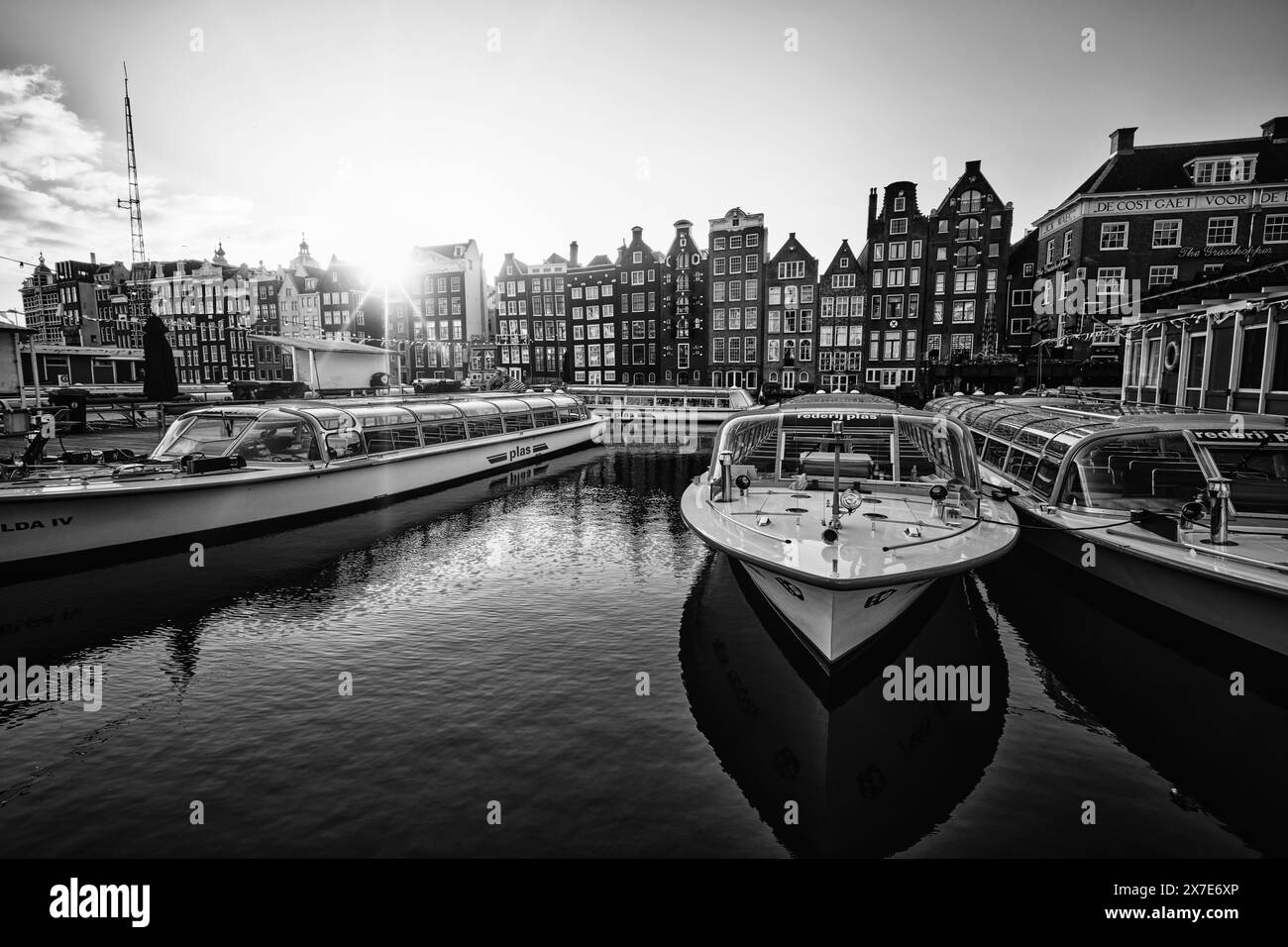 Niederlande, Amsterdam - 07. April 2024: Architektur von Amsterdam, historische Apartmenthäuser mit Reflexionen auf dem Wasser und Boote bereit für eine Kanaltour Stockfoto