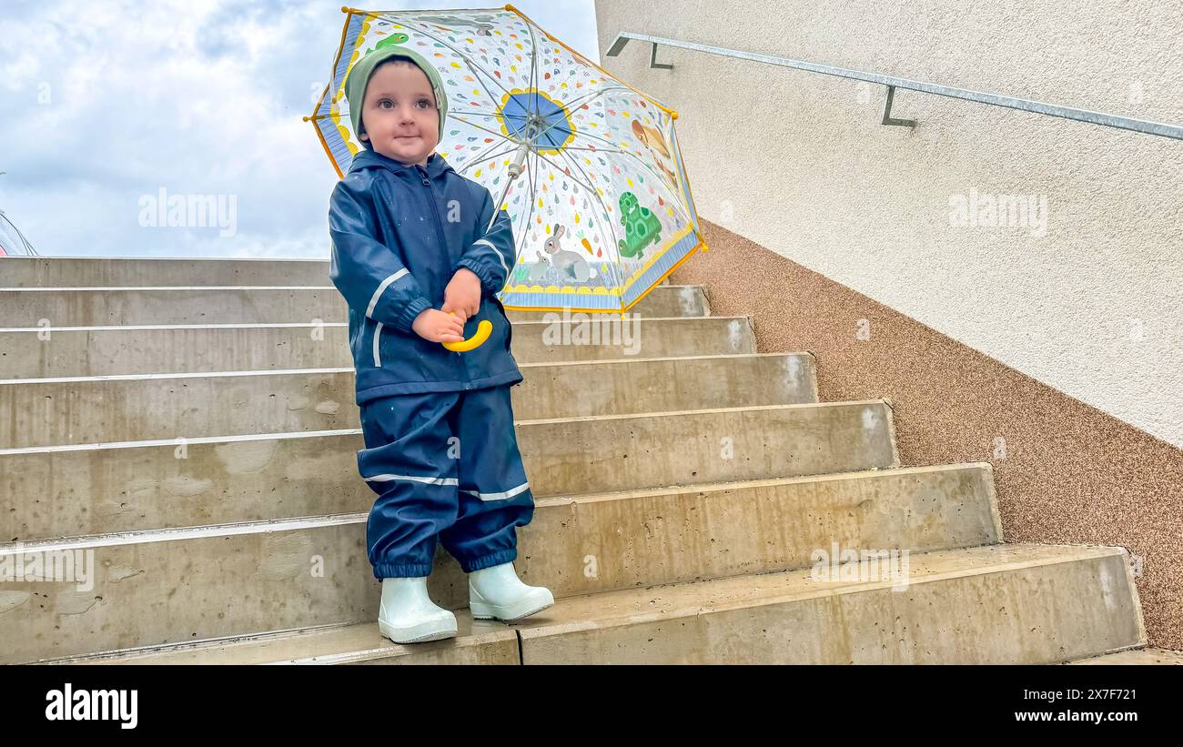 Kinder auf der Treppe tragen Gummistiefel und wasserdichten Anzug mit Regenschirm Stockfoto