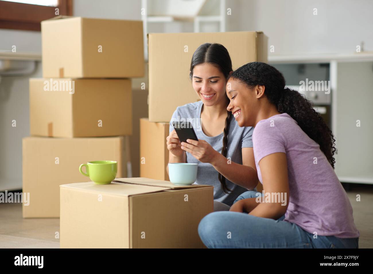 Schwarz-weiße Frauen, die das Telefon überprüfen, ziehen in der Küche um Stockfoto