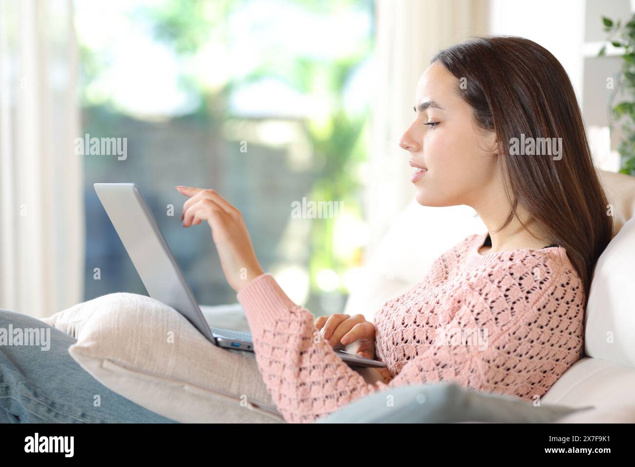 Das Seitenporträt einer Frau verwendet einen Laptop, der zu Hause sitzt Stockfoto