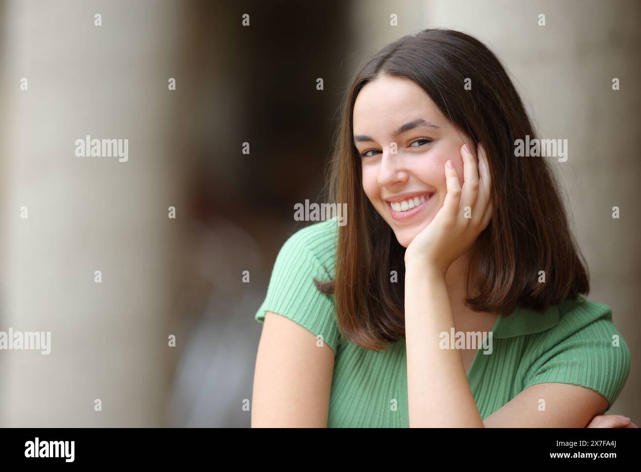 Schöne Frau mit weißem Lächeln, die auf der Straße sitzt, schaut dich an Stockfoto