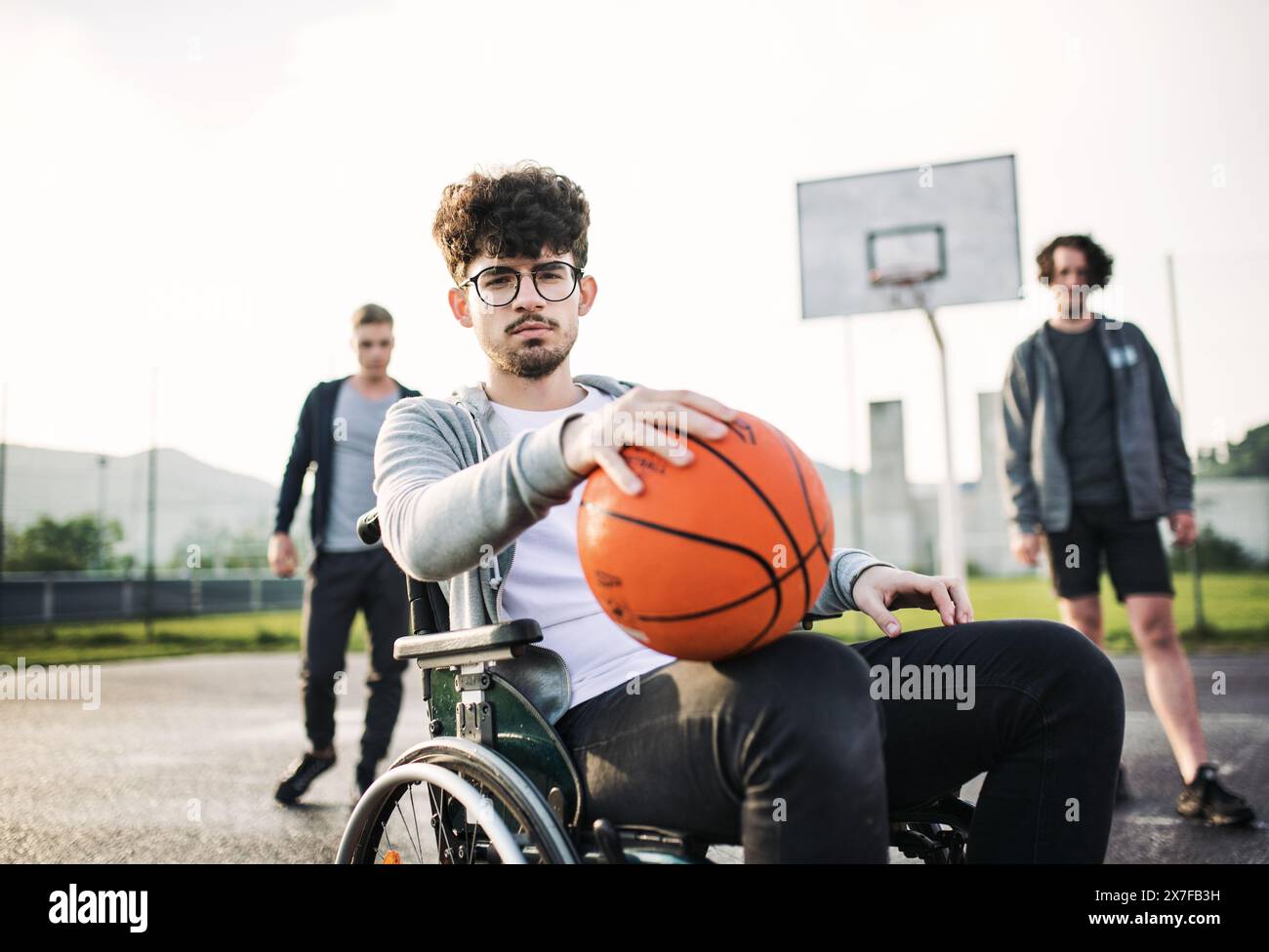 Behinderter junger Mann im Rollstuhl, der mit seinen Freunden Basketball spielt. Teamwrok und männliche Freundschaft. Stockfoto