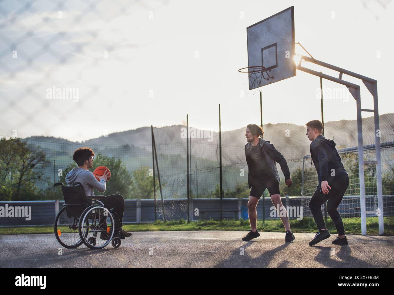 Behinderter junger Mann im Rollstuhl, der mit seinen Freunden Basketball spielt. Teamwrok und männliche Freundschaft. Stockfoto