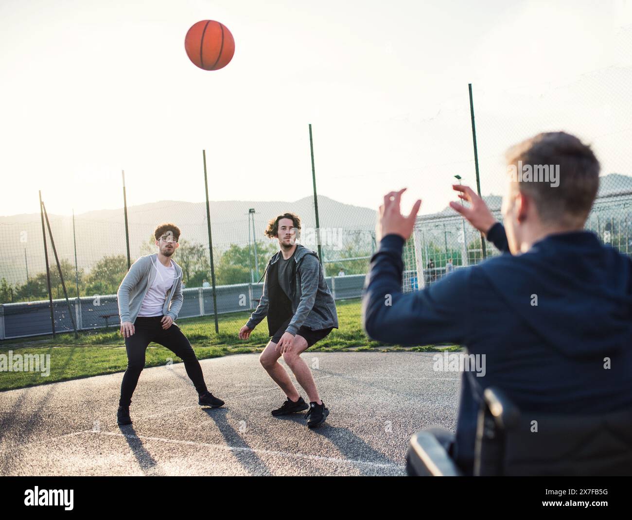 Behinderter junger Mann im Rollstuhl, der mit seinen Freunden Basketball spielt. Teamwrok und männliche Freundschaft. Stockfoto