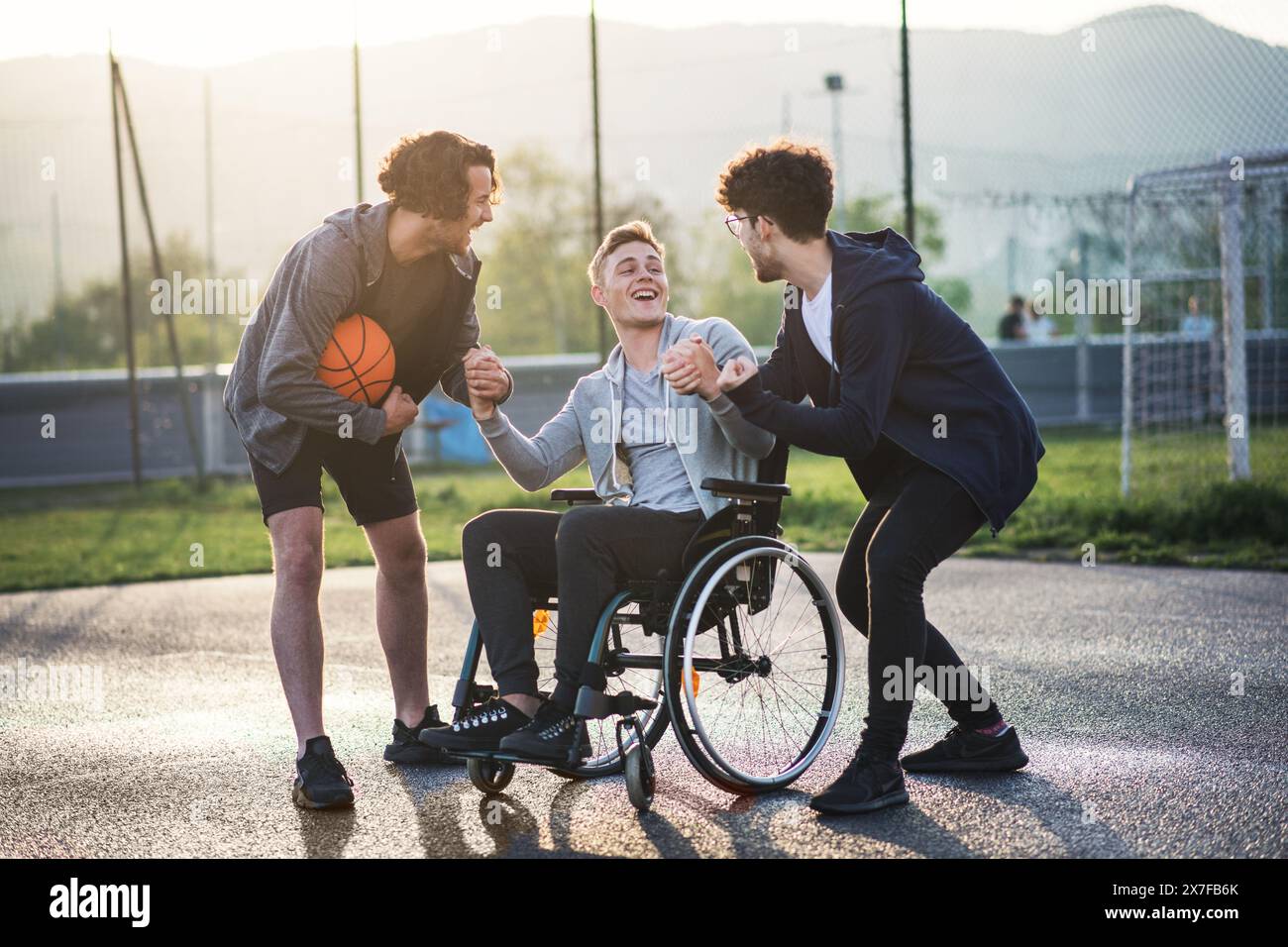 Behinderter junger Mann im Rollstuhl, der mit seinen Freunden Basketball spielt. Teamwrok und männliche Freundschaft. Stockfoto