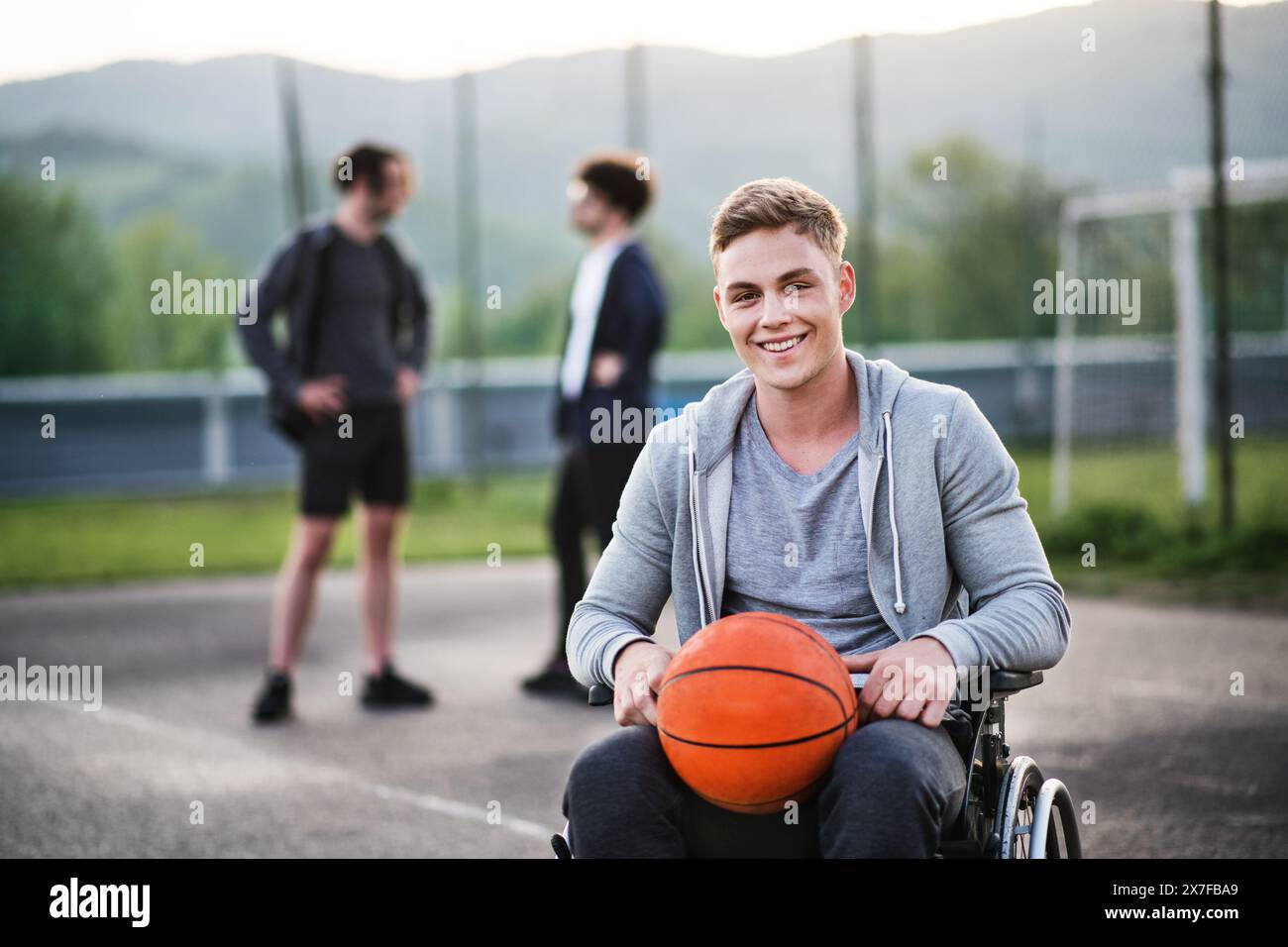 Behinderter junger Mann im Rollstuhl, der mit seinen Freunden Basketball spielt. Teamwrok und männliche Freundschaft. Stockfoto