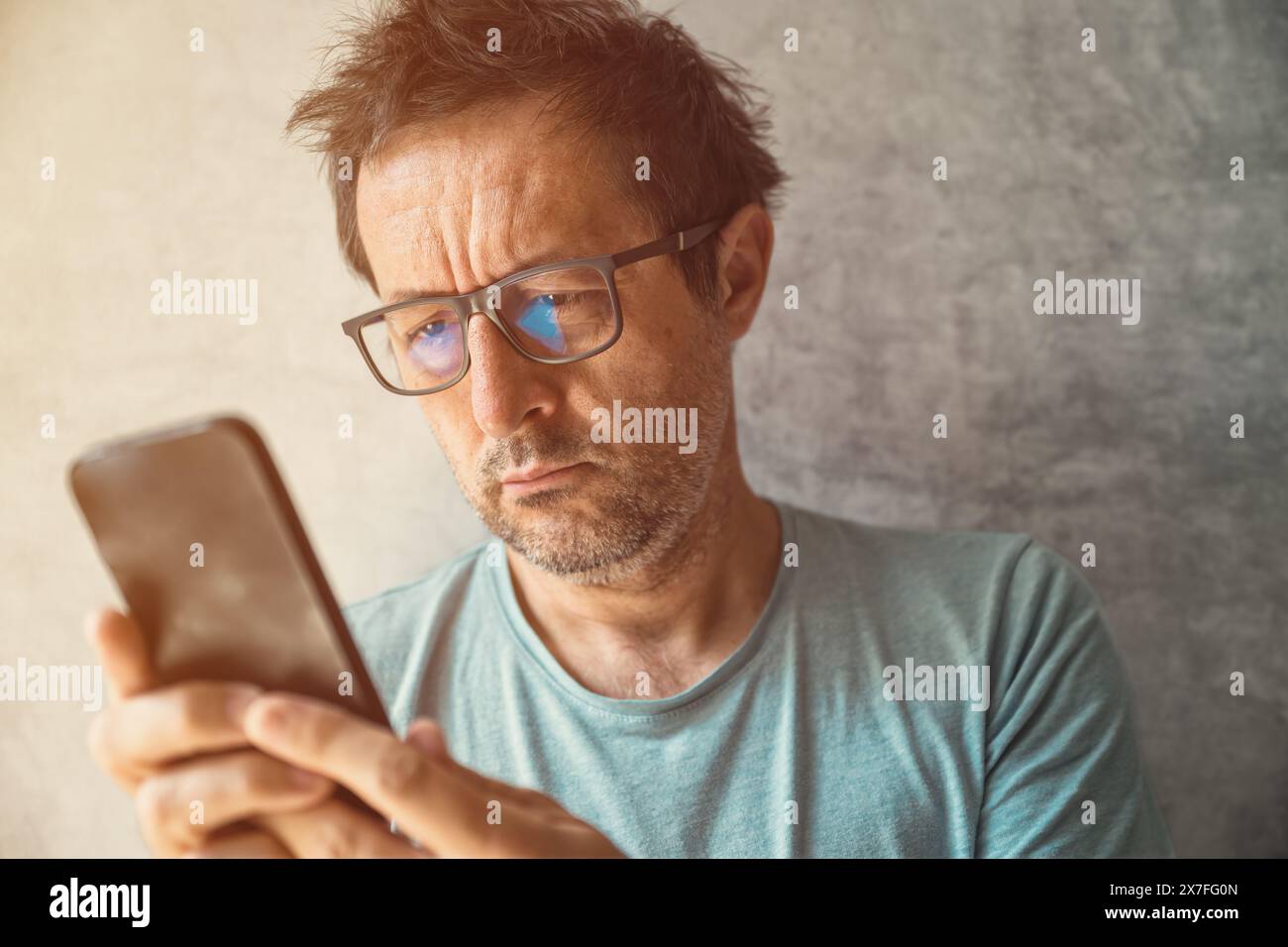 Porträt eines lässigen, authentischen, erwachsenen Mannes mit Brille mit Smartphone in Innenräumen, selektiver Fokus Stockfoto