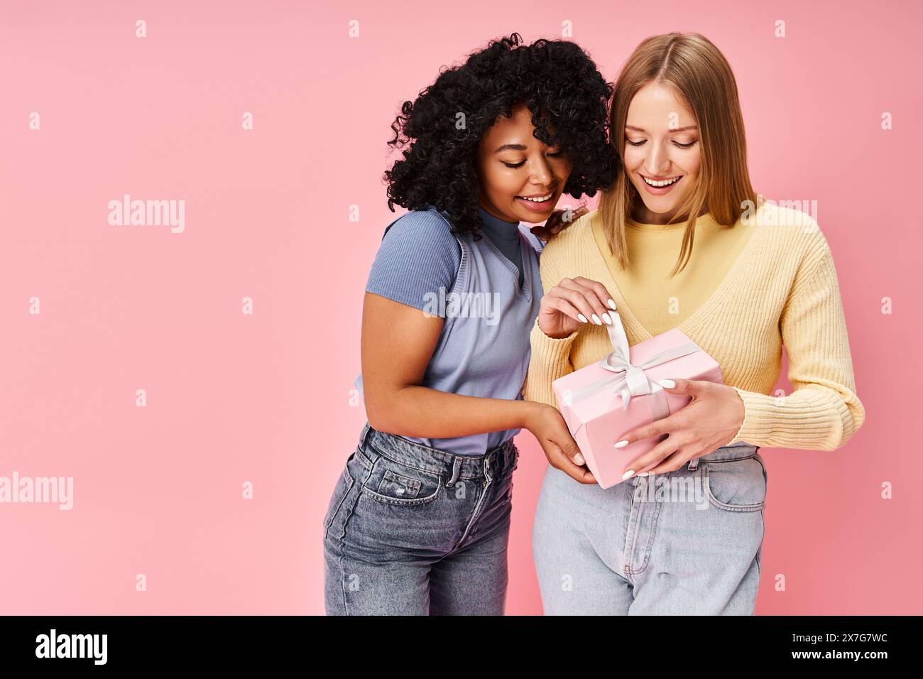 Zwei verschiedene Frauen in kuscheliger Kleidung stehen zusammen und halten ein Geschenk. Stockfoto