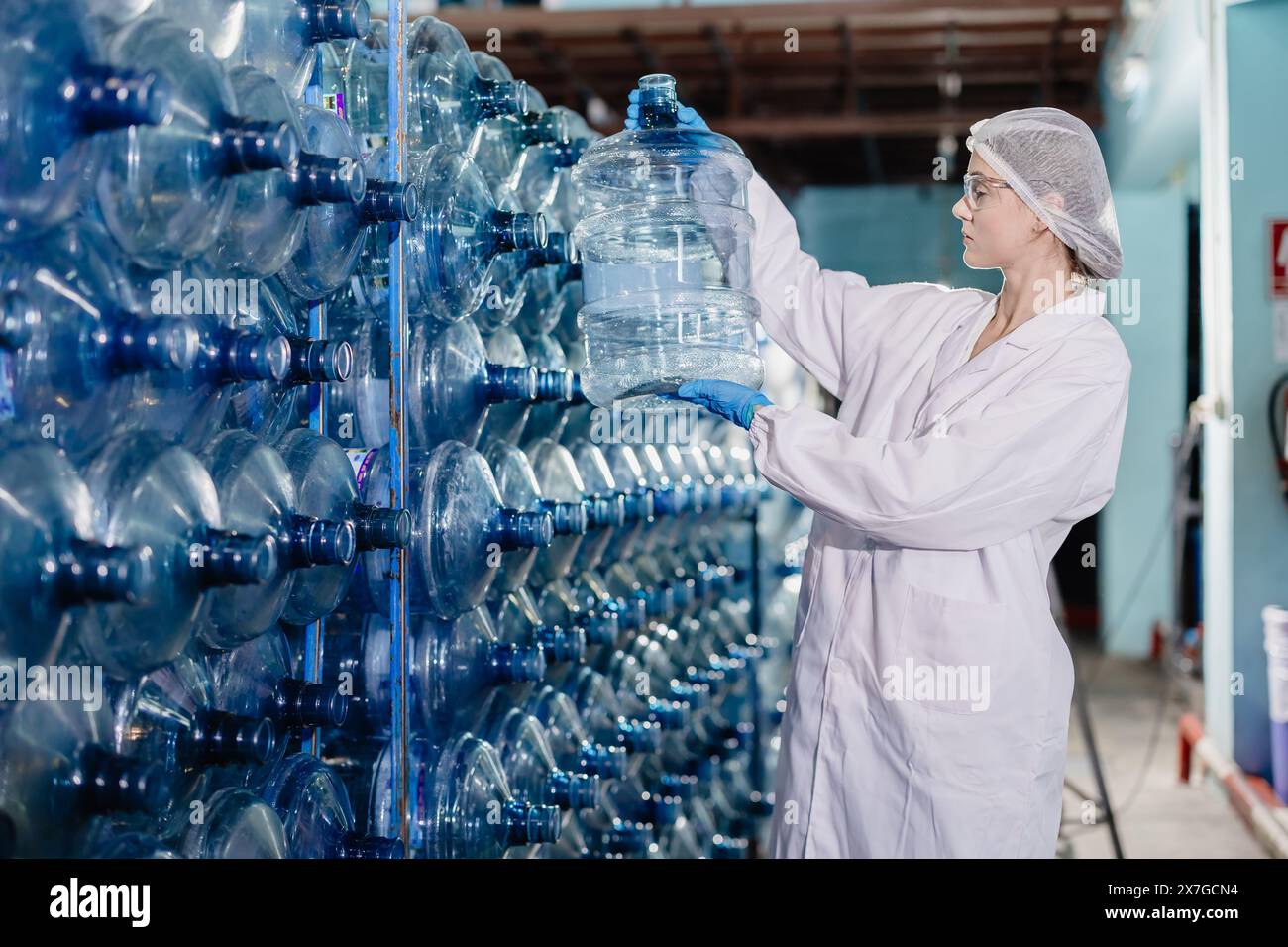 Junge kaukasische Arbeitnehmerinnen arbeiten in Trinkwasserfabrik Zählen Wasserflasche Gallonen-Vorrat an hygienisch einheitlichem Arbeitsplatz Stockfoto