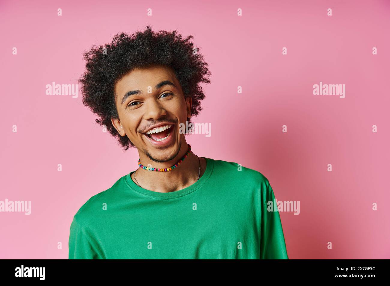 Ein fröhlicher Afroamerikaner mit einem lockigen Afro, der ein grünes Hemd trägt und Emotionen auf rosa Hintergrund ausdrückt. Stockfoto