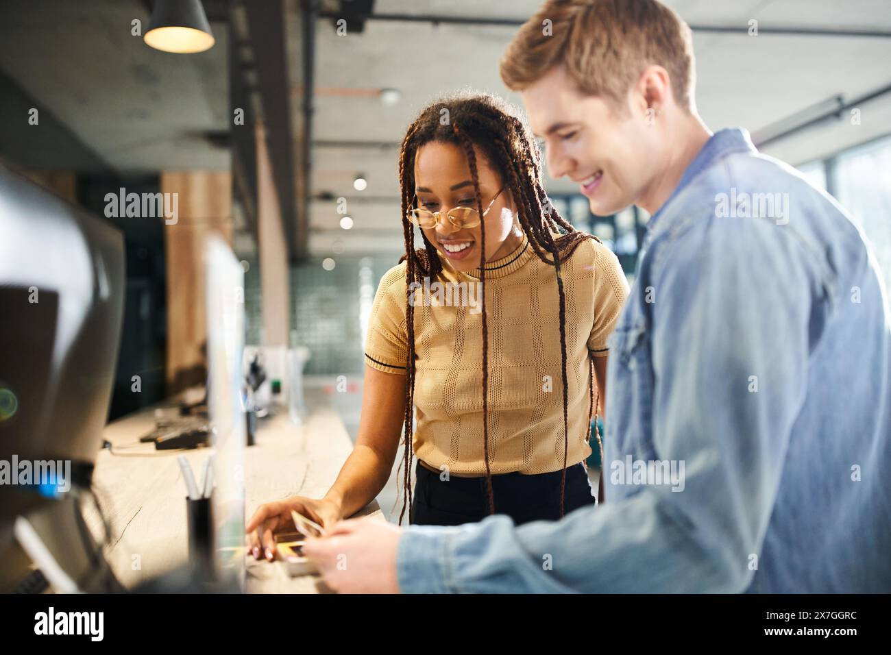 Ein multikultureller Mann und eine Frau in lässiger Kleidung sehen sich während einer Geschäftsreise gemeinsam eine Visitenkarte in einer Hotellobby an. Stockfoto