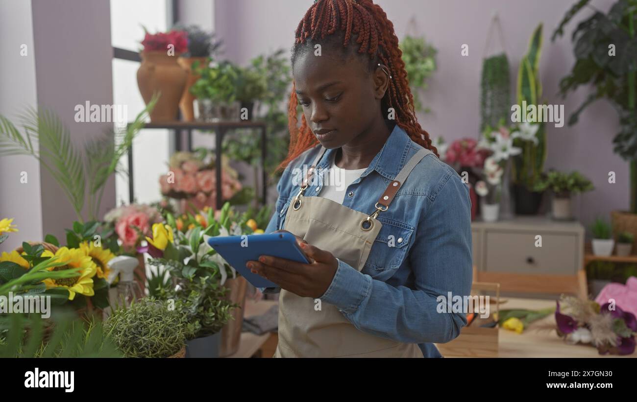 Eine junge afroamerikanerin, die eine Tablette in einem bunten Blumenladen benutzt Stockfoto
