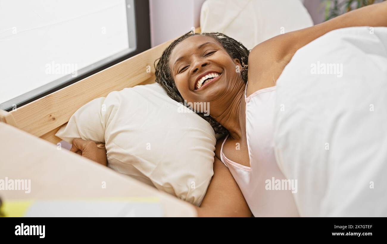 Eine fröhliche afroamerikanische reife Frau, die zu Hause im Bett liegt und Glück und Trost ausstrahlt. Stockfoto