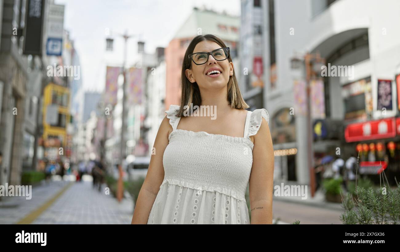 Schönheit, atemberaubende Erwachsene hispanische Frau mit Brille und Blick auf das pulsierende Stadtbild tokios. Dieser brünette Tourist ist fasziniert von Stockfoto