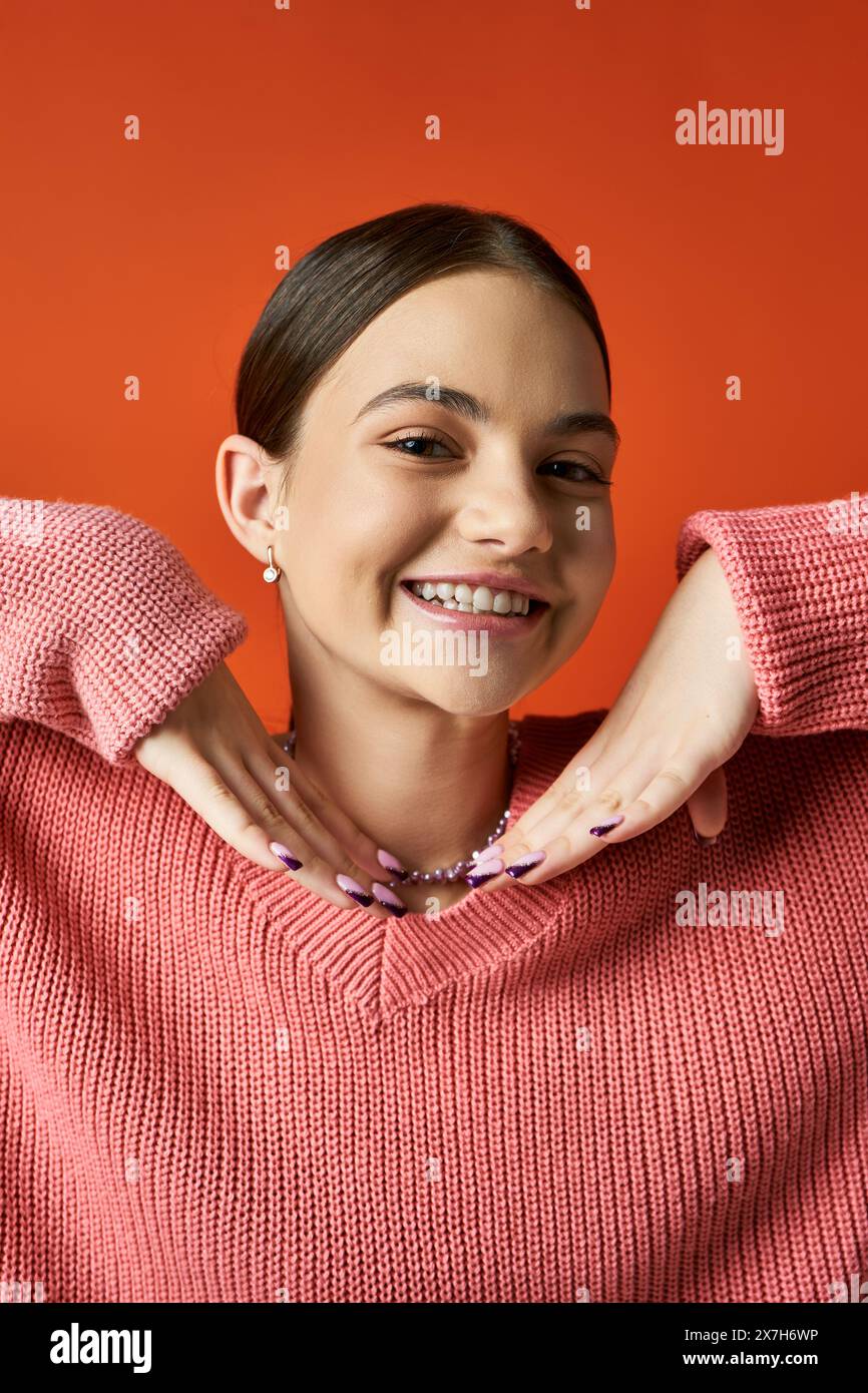 Ein brünettes Teenager-Mädchen in einem rosa Pullover lächelt vor einem orangen Hintergrund in einem Studio. Stockfoto