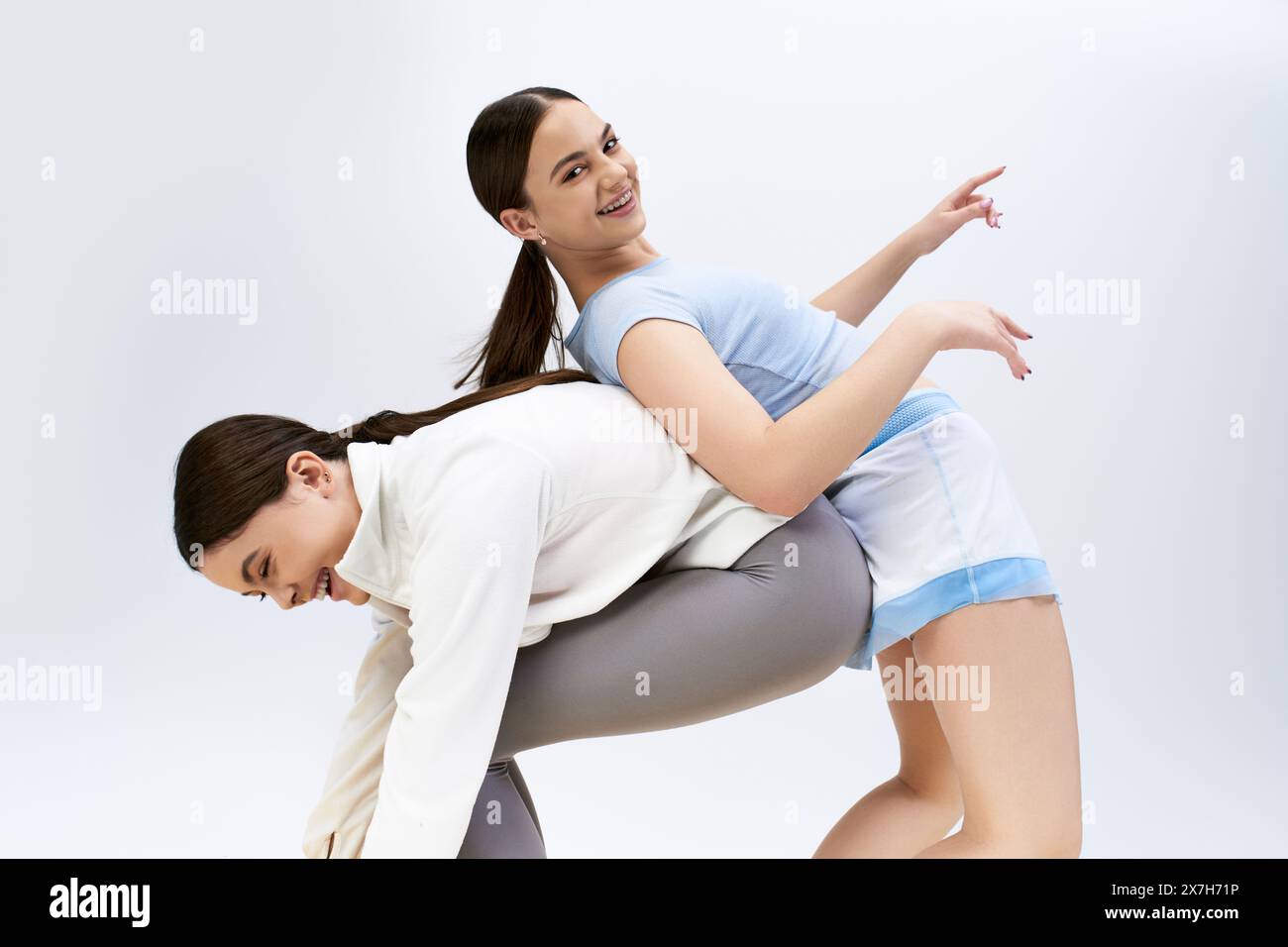 Zwei hübsche, brünette Teenager-Mädchen in sportlicher Kleidung zeigen ihre Tanzbewegungen in einem Studio vor grauem Hintergrund. Stockfoto