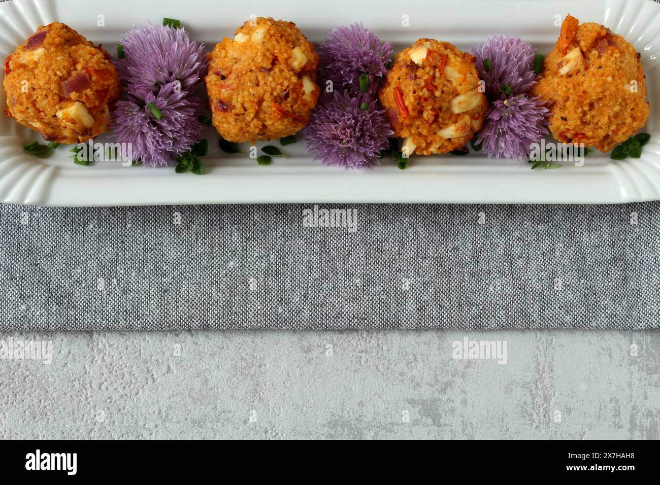 Couscous-Feta-Kugeln mit Schnittlauchblüten auf neutralgrauem Hintergrund Stockfoto
