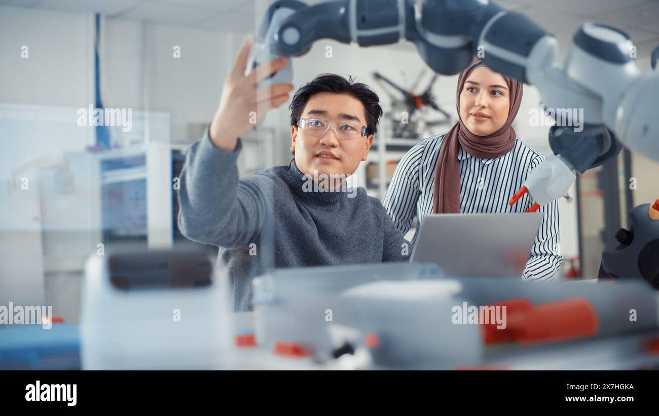 Arab Female Future Engineer beschäftigt sich mit der Arbeit eines geschickten Entwicklers. Asian man erklärt Grundprinzipien und Examine Robotic Arm. Analyse und Evaluation von Prototypen und Robotersystemen. Stockfoto