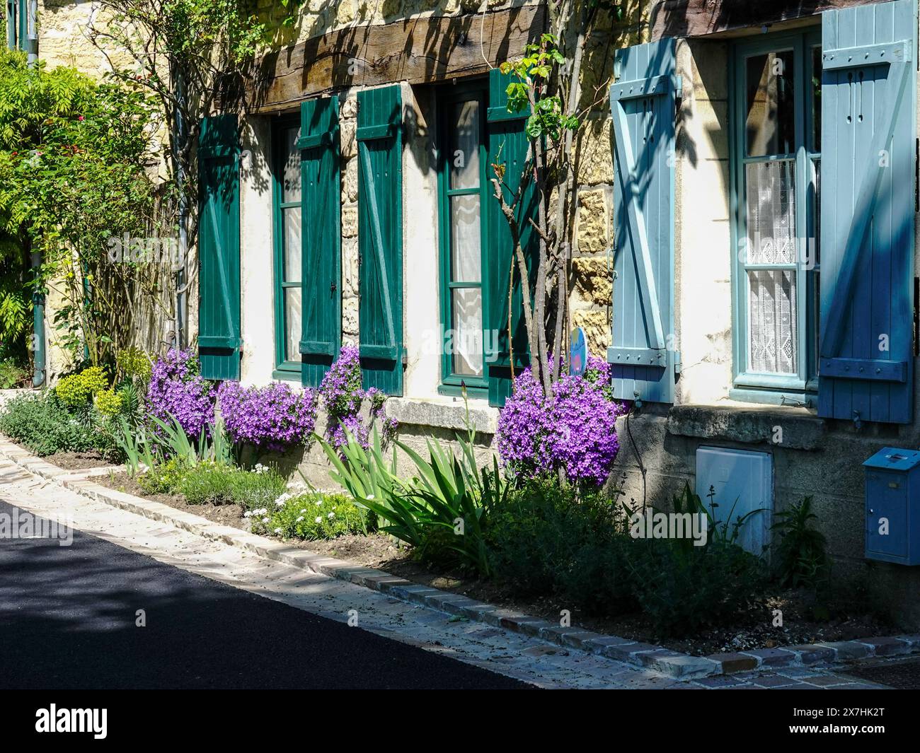Charmantes, restauriertes Steingebäude mit bunten Fensterläden und bunten Pflanzen, Rue Daubigny, Auvers-sur-Oise, Frankreich. Stockfoto