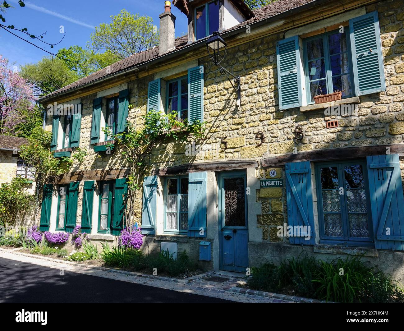 Charmantes, restauriertes Steingebäude mit bunten Fensterläden und bunten Pflanzen, Rue Daubigny, Auvers-sur-Oise, Frankreich. Stockfoto