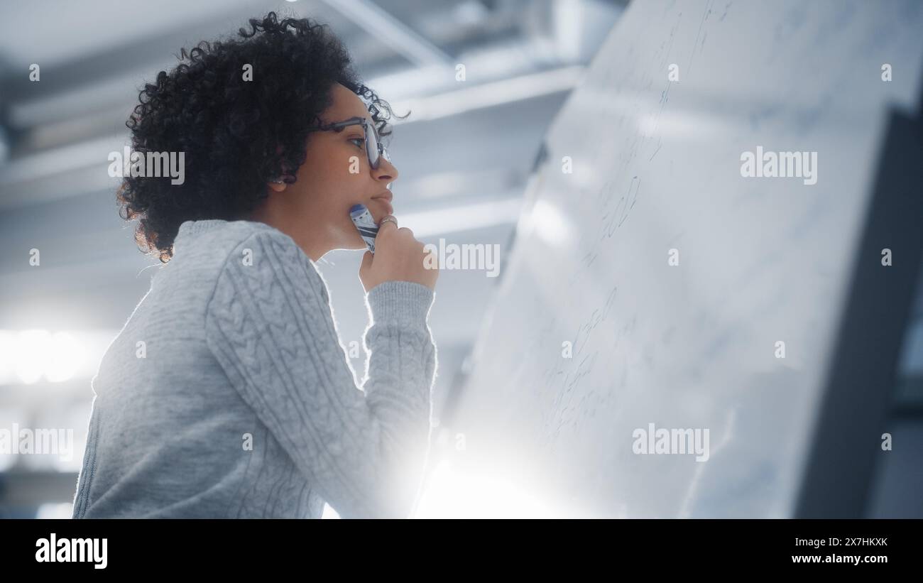 Schwarze Wissenschaftlerin löst Probleme und schreibt komplizierte mathematische Gleichungen auf dem Whiteboard. Genius, Konzeptualität und Durchbruch in Wissenschaft und Technologie. Stockfoto