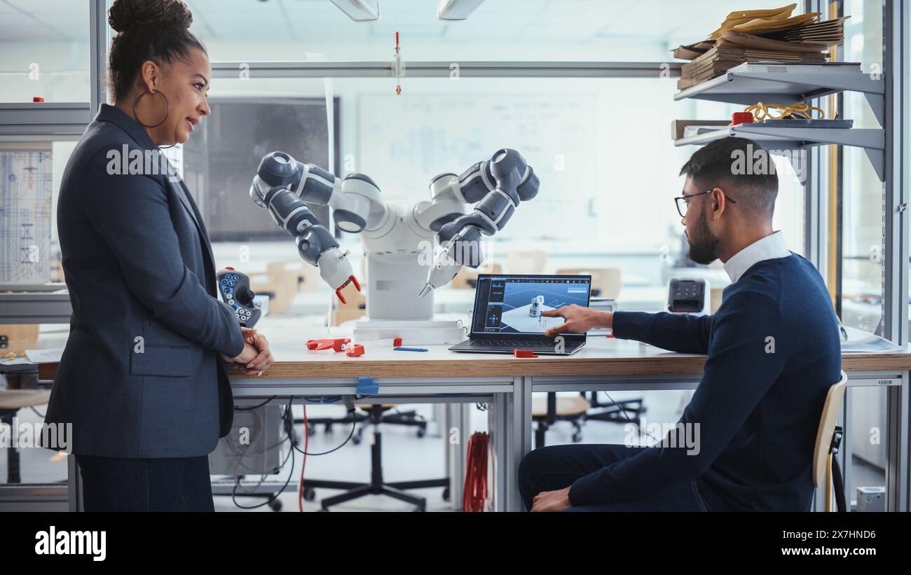 Schwarzer Chefingenieur diskutiert Futuristic Robotic Arm mit einem jungen vielversprechenden männlichen Computerwissenschaftler mit Laptop im Forschungslabor. Innovatives Startup Company-Konzept. Mittlere Aufnahme. Stockfoto