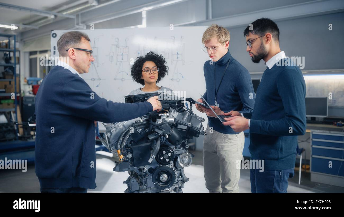Chefingenieur erklärt den jungen Spezialisten die Technik und weist auf Whiteboard auf. Intelligente Menschen, die Probleme lösen und sich den Motor ansehen. Ingenieurwesen und umweltfreundliche elektrische Energietechnologie. Stockfoto