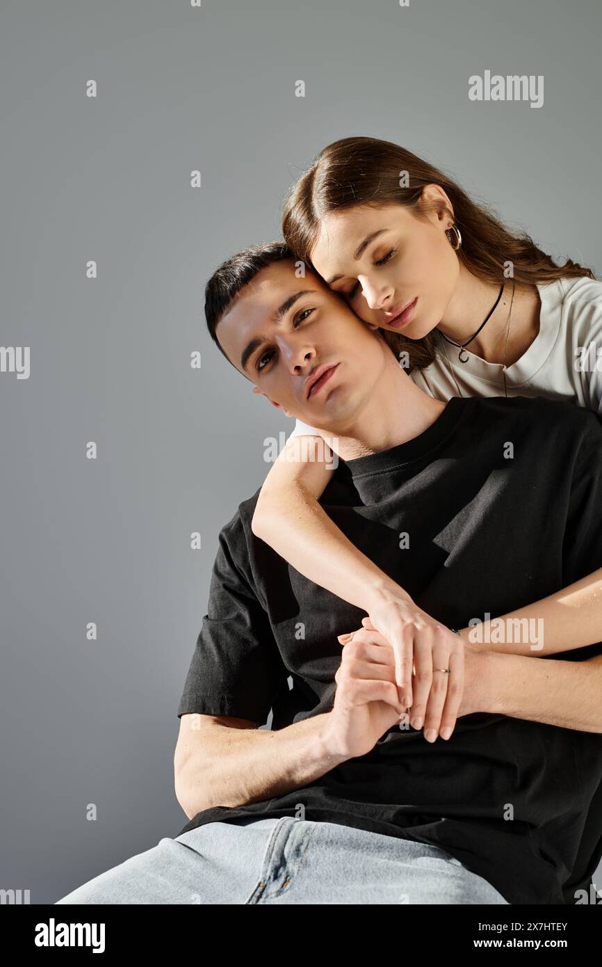 Ein Mann zeigt seine Stärke und Liebe, indem er eine Frau auf dem Rücken vor einem grauen Studio-Hintergrund trägt. Stockfoto