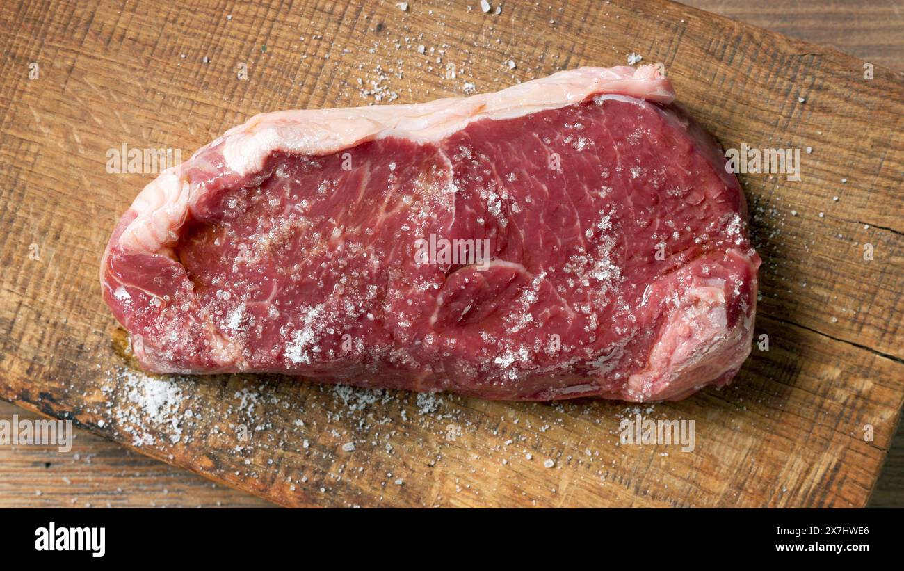 Frisches rohes Steak mit Salz auf hölzernem Schneidebrett, Blick von oben Stockfoto
