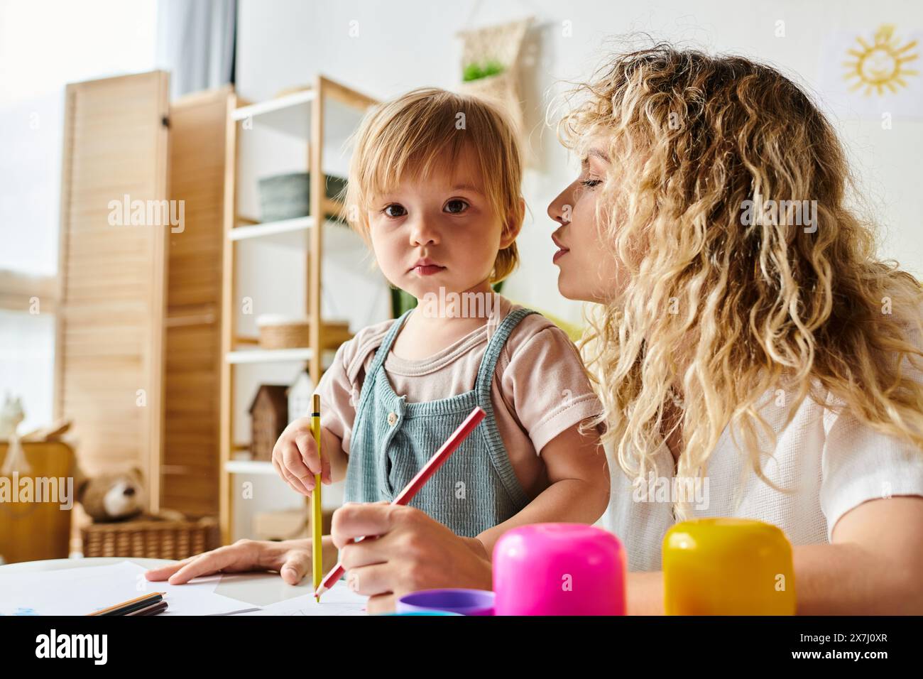 Eine lockige Mutter und ihre Kleinkind-Tochter üben die Montessori-Methode der Erziehung an einem Tisch aus. Stockfoto
