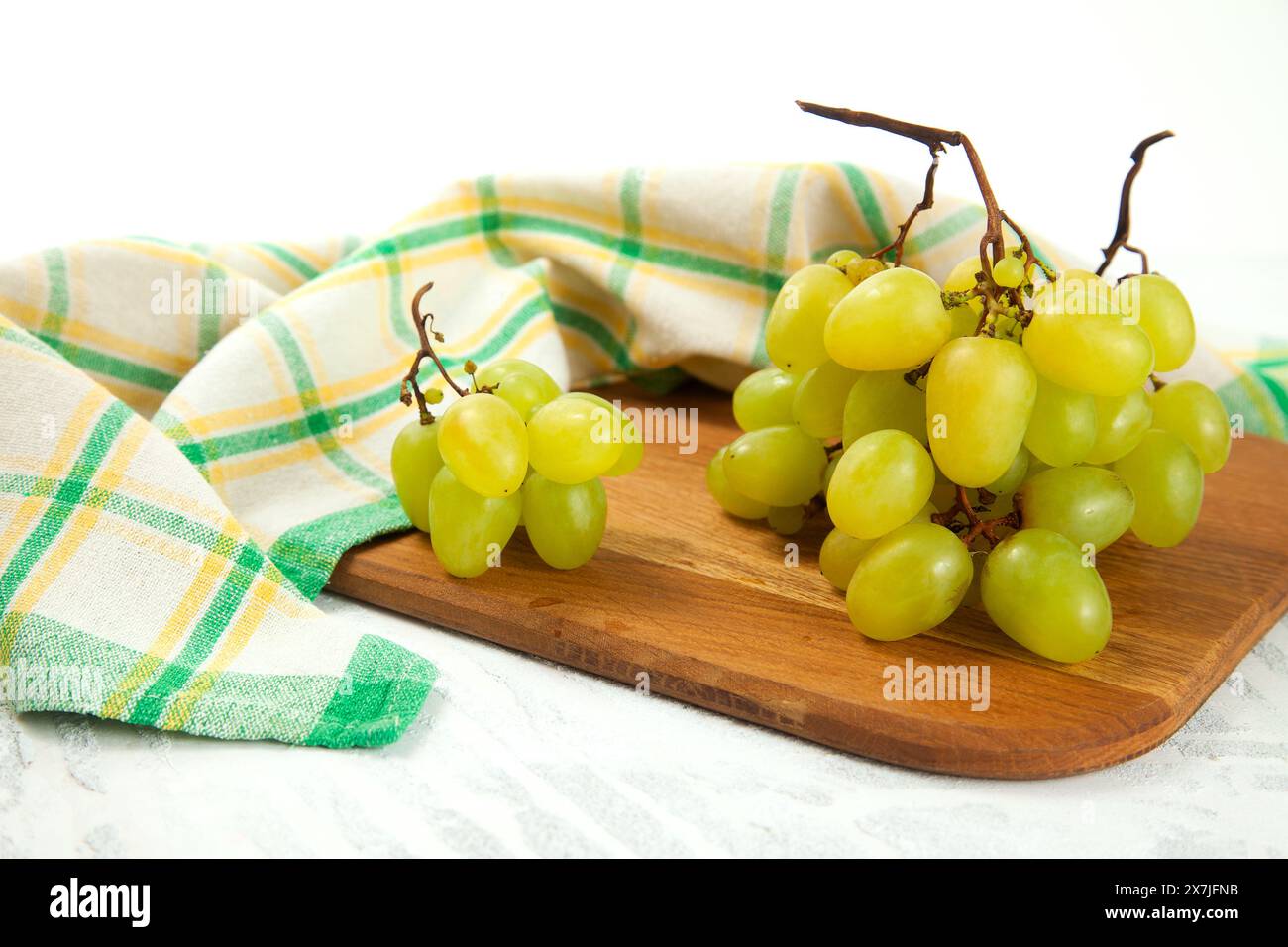 Schneidebrett mit einem großen Haufen reifer grüner Trauben auf weiß. Weißweintrauben mit grünem Küchentuch auf weißem hölzernem Hintergrund. Stockfoto