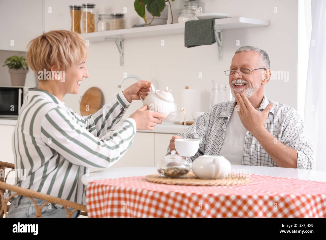 Reifes, taubes, stummes Paar, das Tee an den Tisch in der Küche gießt Stockfoto