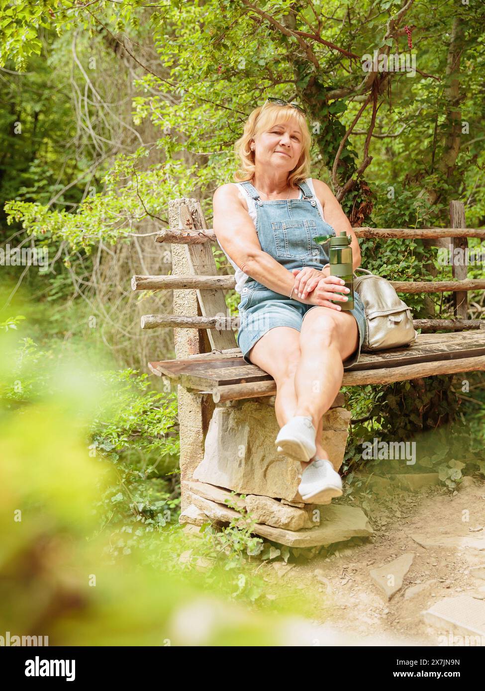 Frau, die Wasser aus wiederverwendbarer Trinkflasche im Wald trinkt Stockfoto