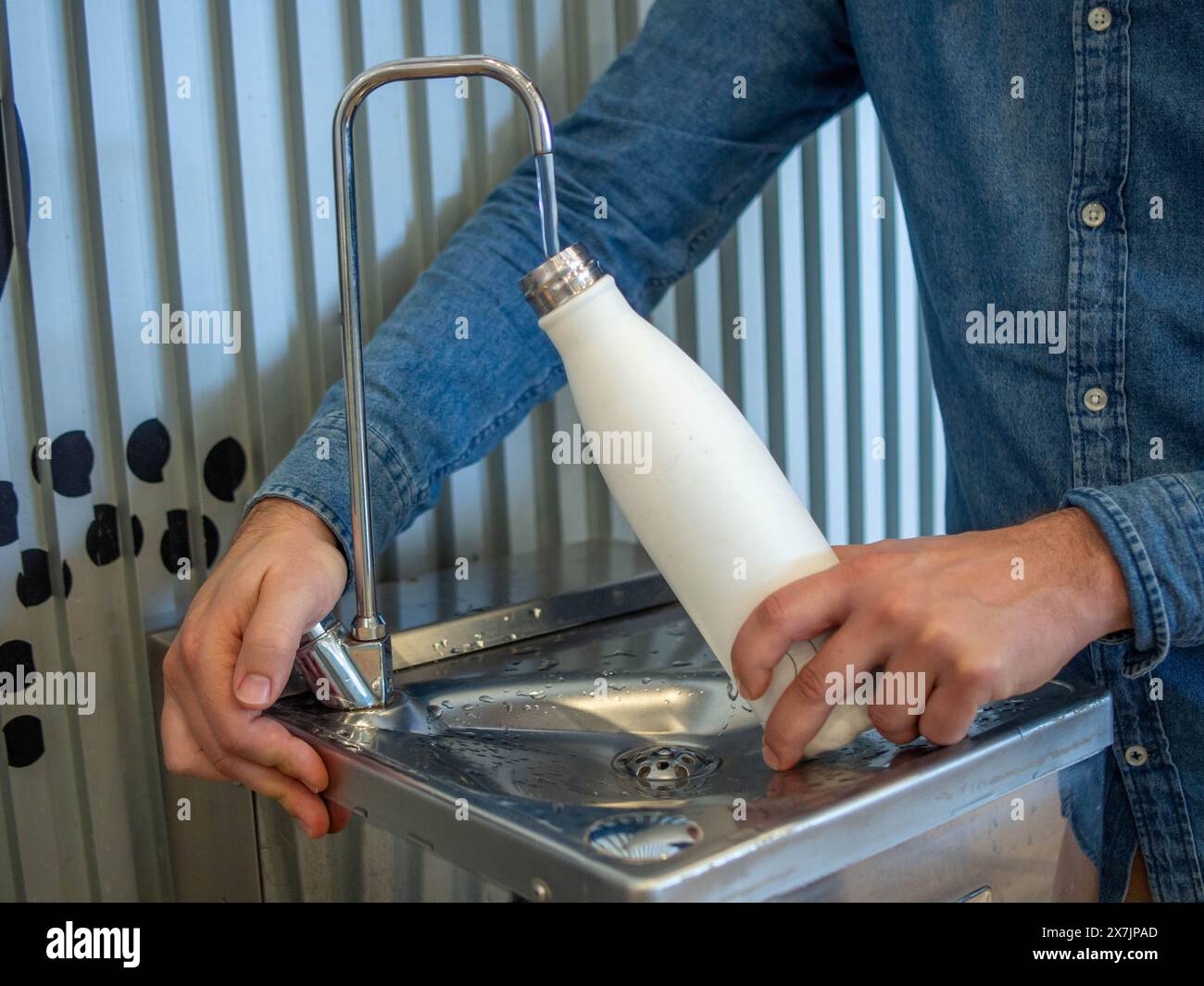 Ein junger Mann, der seine wiederverwendbare Flasche an einem Flughafenbrunnen füllt Stockfoto