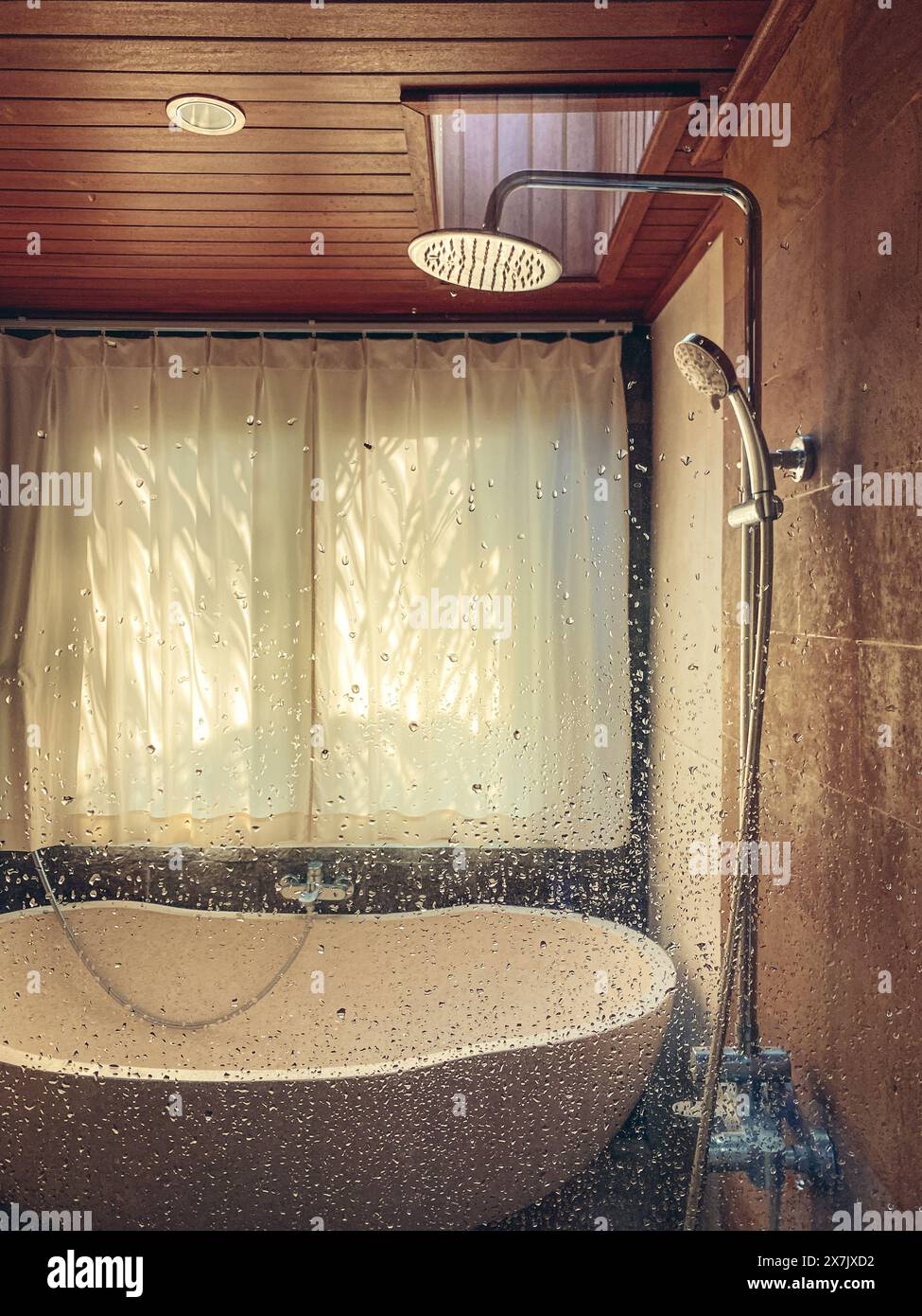 Dusche und Steinbadewanne im Badezimmer mit Fenster und Wassertropfen auf Glas Stockfoto