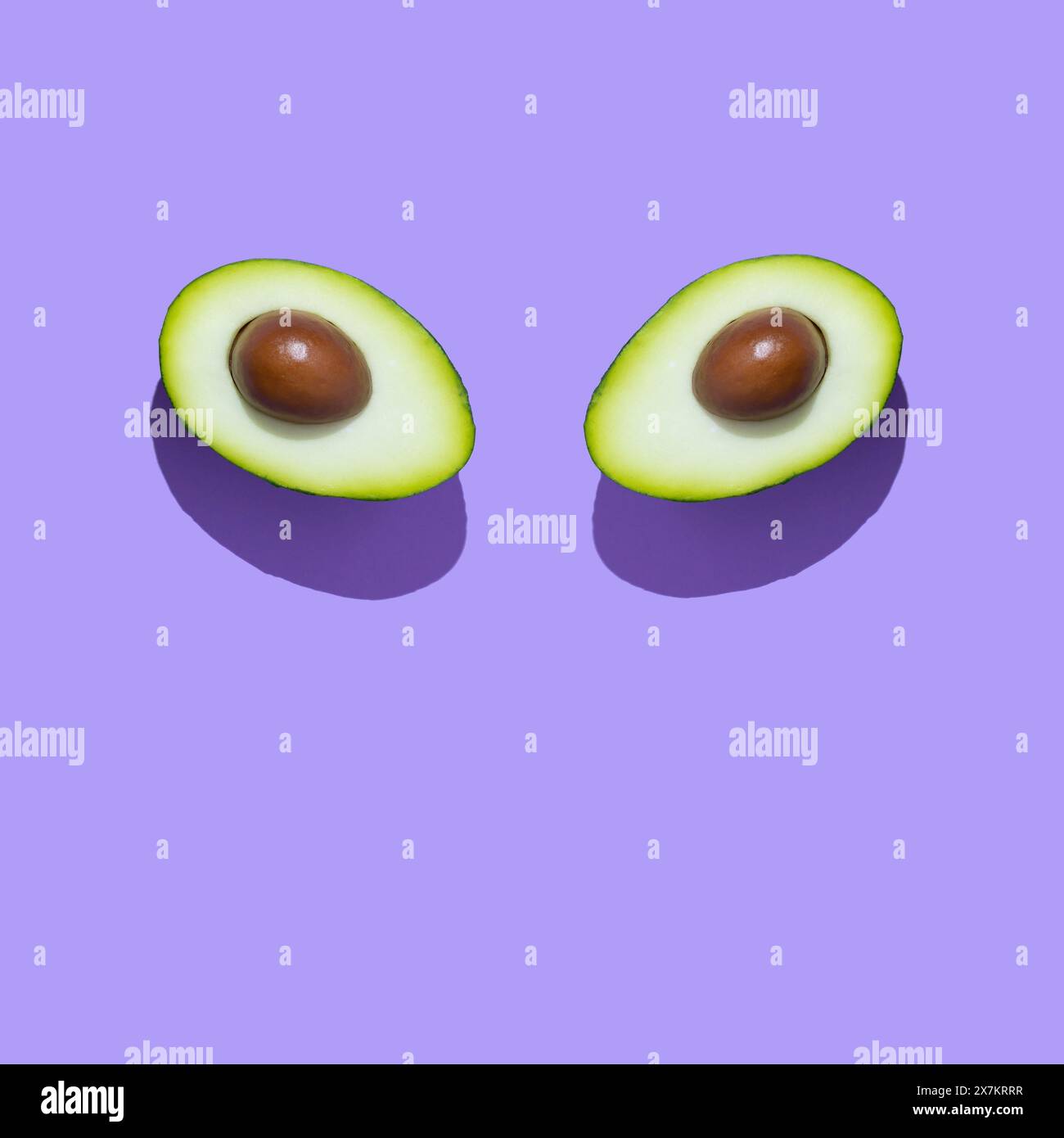 Frisch geschnittene Avocadoform wie Augen isoliert auf violettem Hintergrund. Minimales surreales Essenskonzept. Trendiges und lustiges Sommerobst. Flache Lagen. Stockfoto