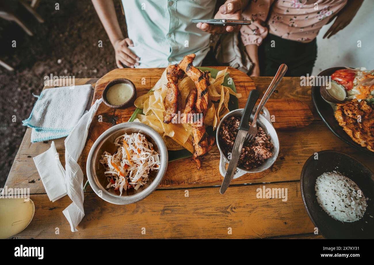 Person, die ein traditionelles Roastbeef mit Bananenscheiben und Gallopinto auf einem Holztisch isst. Nahaufnahme von traditionellem Bratfleisch und Stockfoto