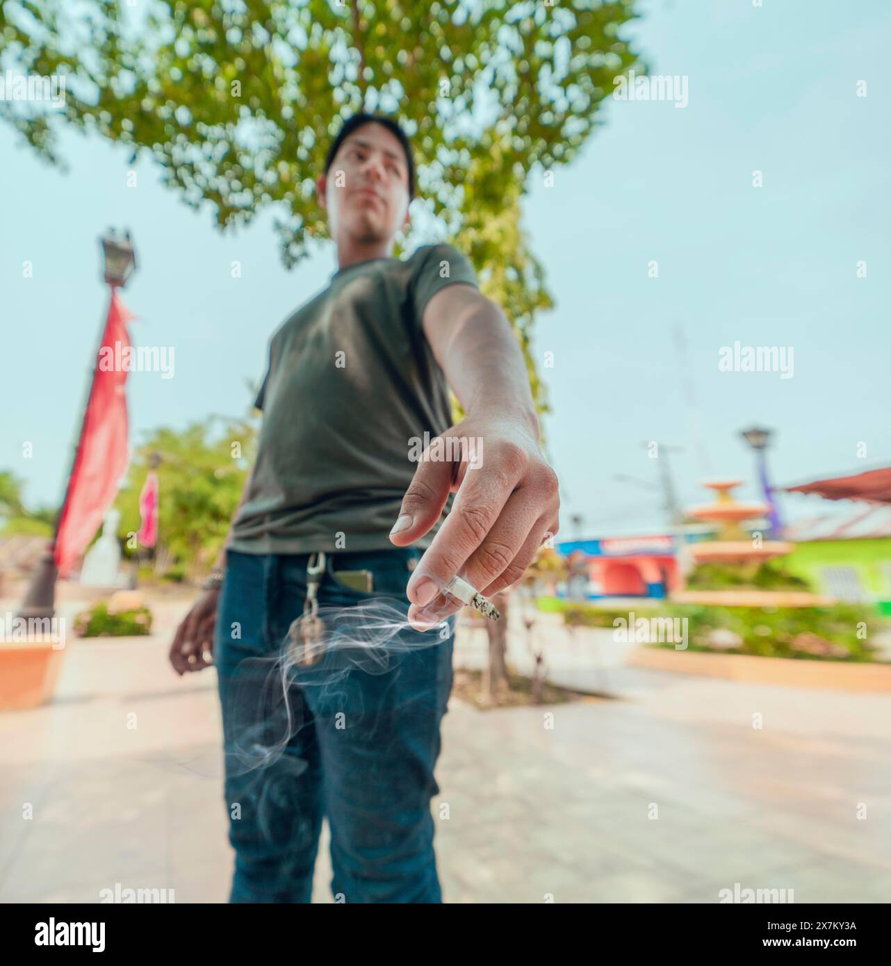 Porträt von Typ, der auf der Straße raucht. Nahaufnahme eines jungen Mannes, der eine brennende Zigarette auf der Straße zeigt Stockfoto