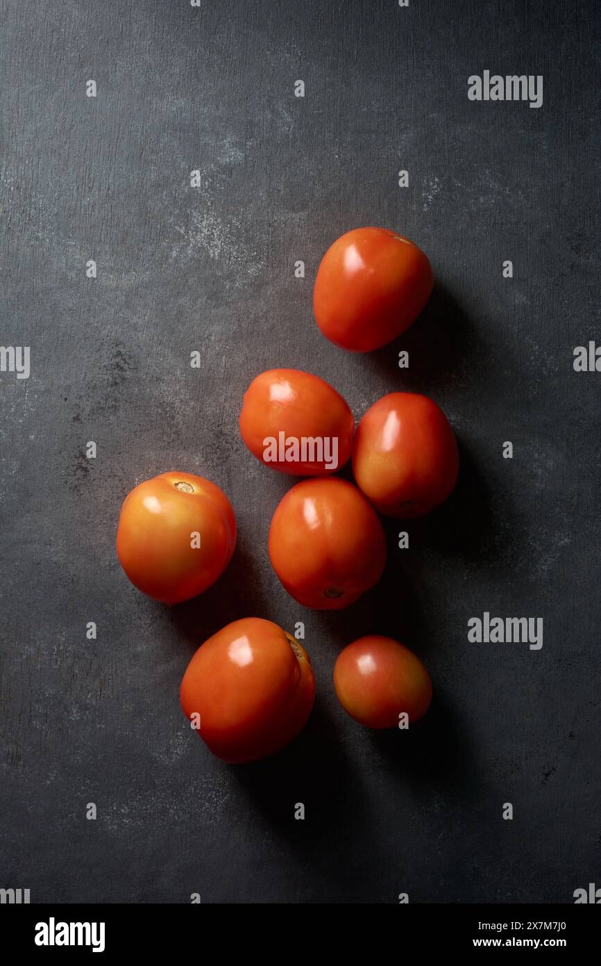 Tomaten auf schwarzem texturiertem Hintergrund, rötlich-orange gereifte reife Früchte, dunkle stimmungsvolle Lebensmittelfotografie mit Kopierraum von oben aufgenommen Stockfoto