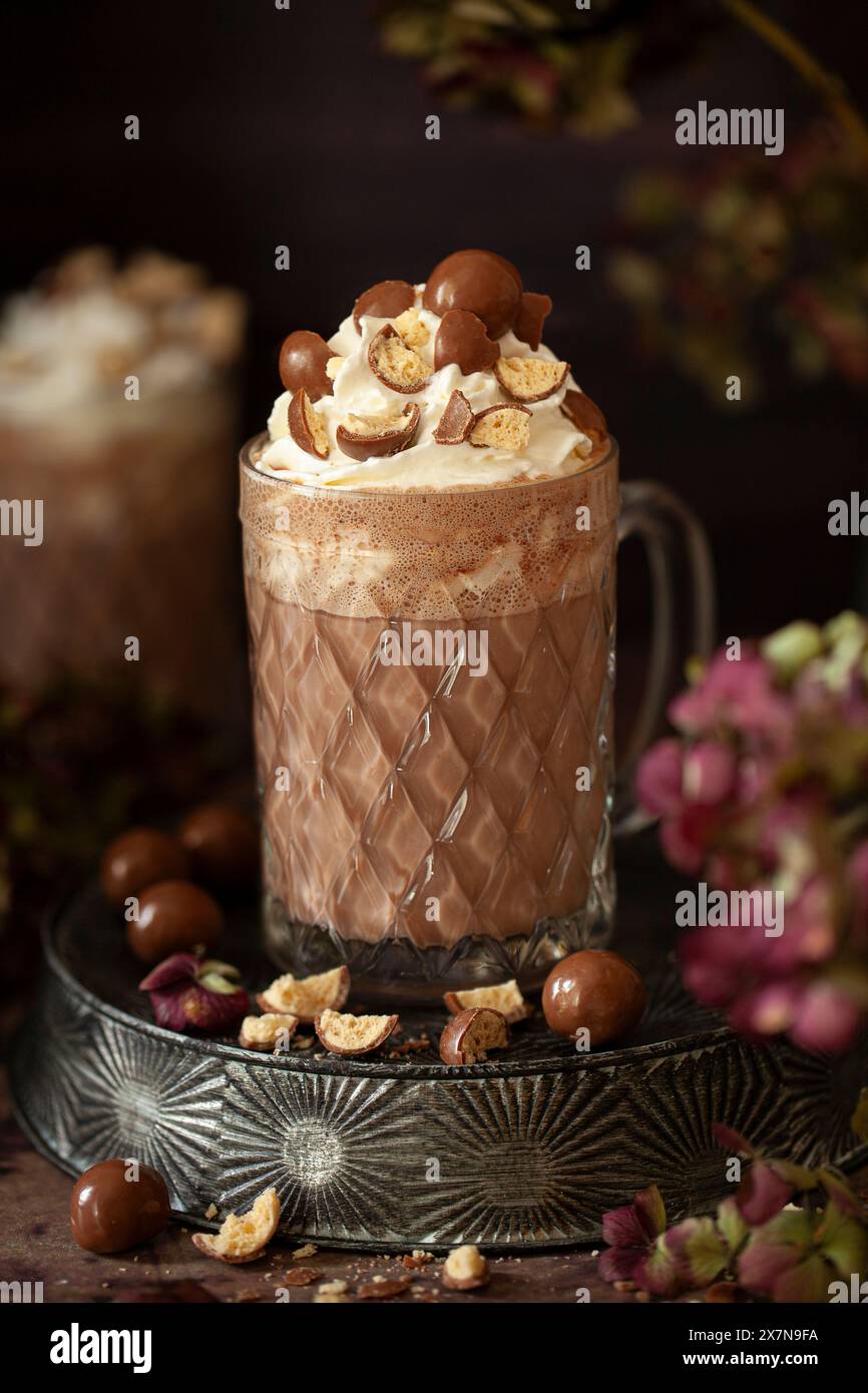 Ein Glasbecher mit gemalzter heißer Schokolade, garniert mit Creme- und Chocolate-Malzbällchen. Stockfoto
