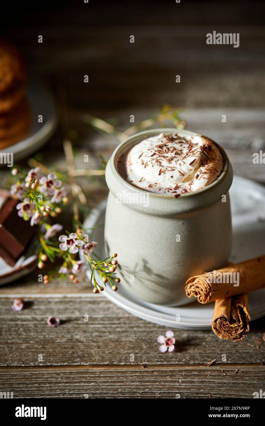 Mexikanische heiße Schokolade mit Schlagsahne auf dunklem Holzhintergrund mit Blumen, Keksen und Zimtstangen. Stockfoto