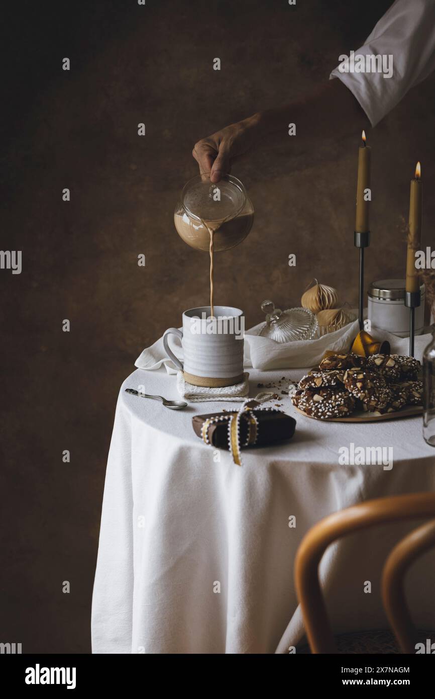 Frau, die heißen Tee aus der Teekanne in eine Tasse gießt. Franginpane Kekse und Kerzenlicht. Frühstück am Morgen oder Teezeit in gemütlichem Haus. Hygge, warm, autu Stockfoto