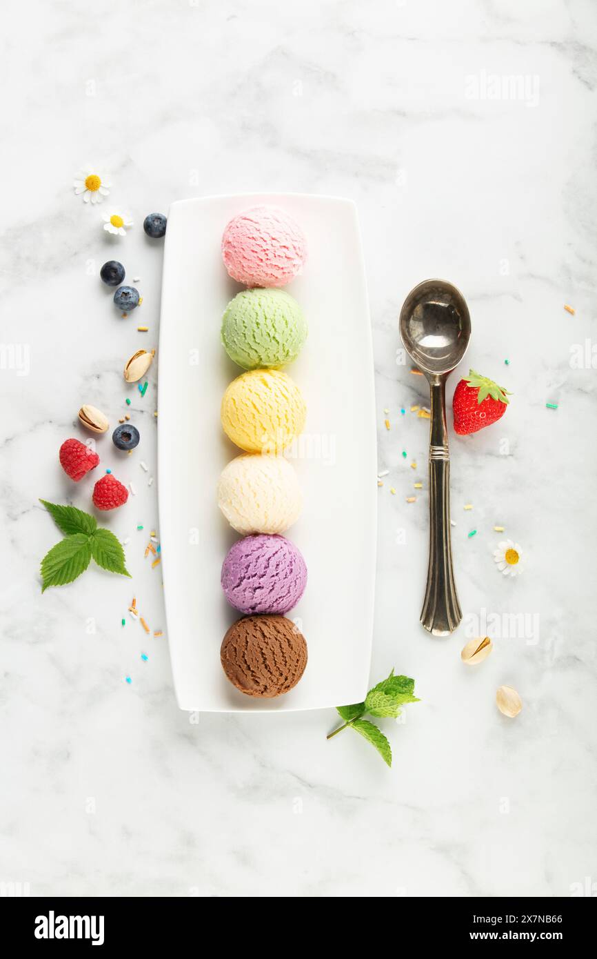Set aus verschiedenen Eislöffeln und Beeren auf weißem Marmorhintergrund. Erdbeere, Pistazien, Mango, Vanille, Heidelbeere und Schokoladeneis. Oben Stockfoto