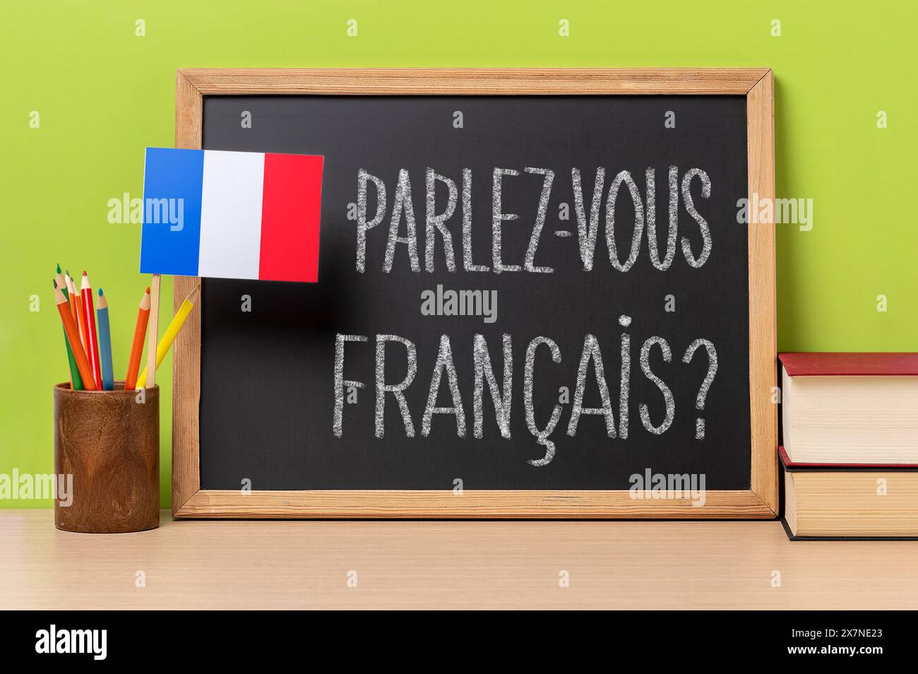 Eine Tafel mit der Frage parlez-vous francais? Sprichst du französisch? Auf französisch geschrieben, ein Topf mit Bleistiften und die Fahne Frankreichs, auf einem hölzernen de Stockfoto